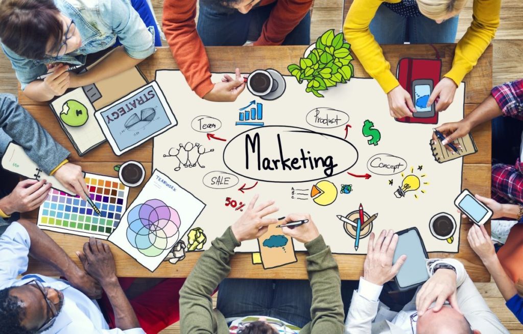 people gathered around a table discussing When to Hire Outsourced Marketing vs. In-House Marketing 