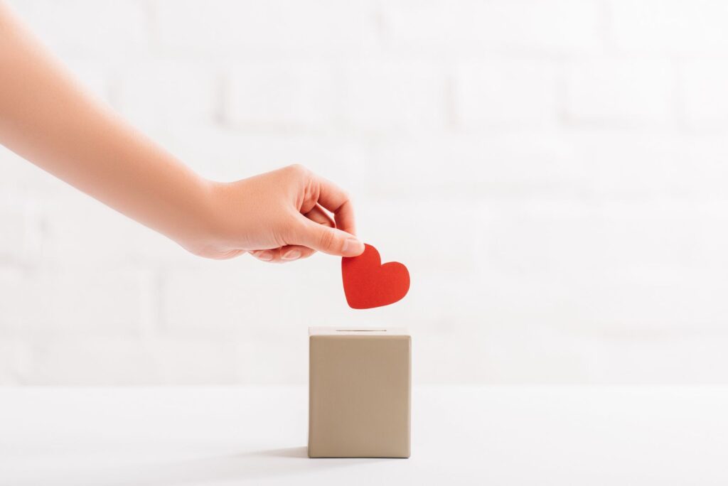 Hand dropping a small red heart into a cause marketing donation box. 