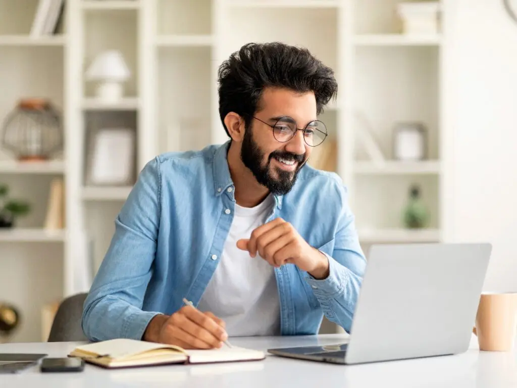 a man sitting at a desk with a laptop and a notebook